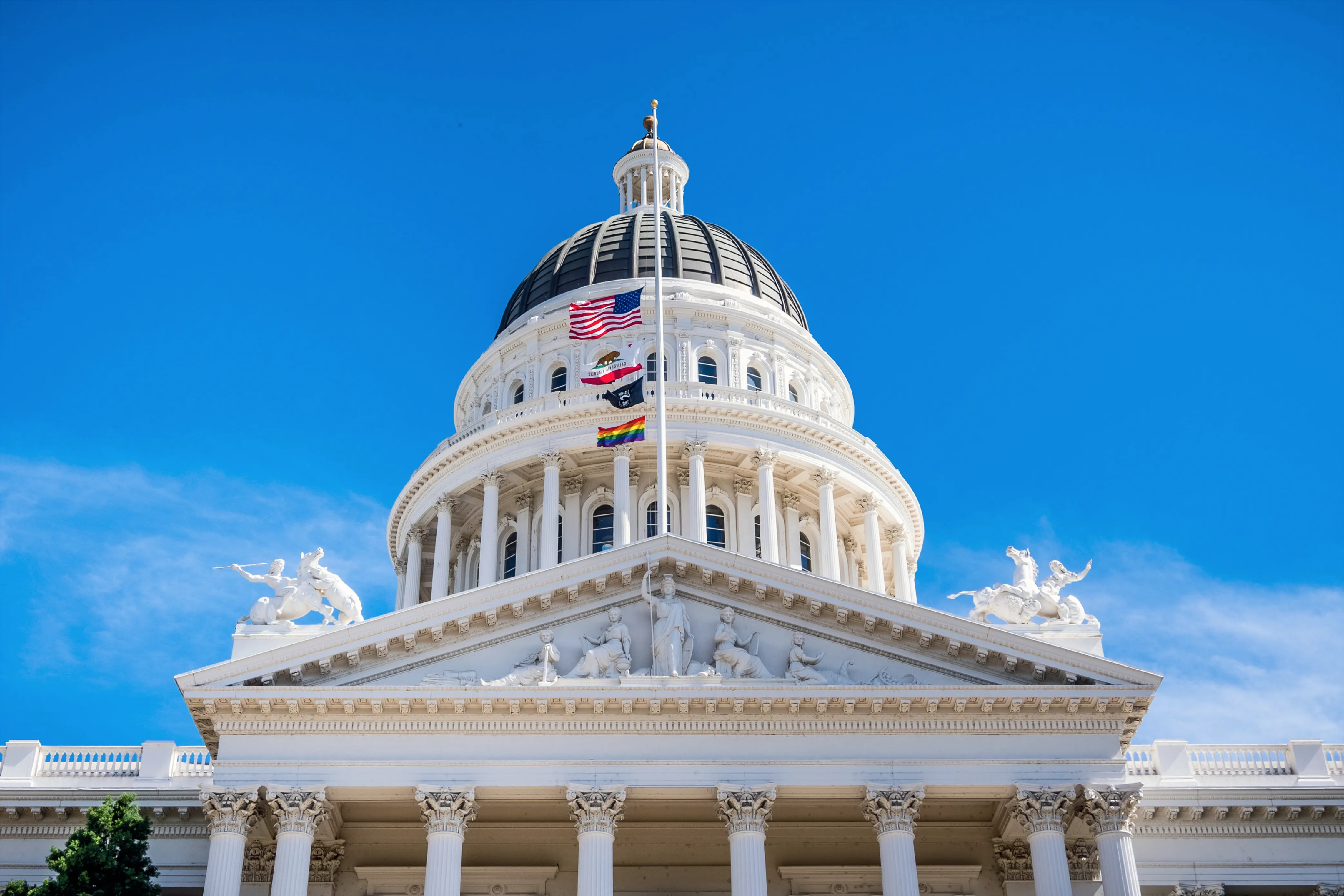 The California State Capitol dome with flags against a blue sky
